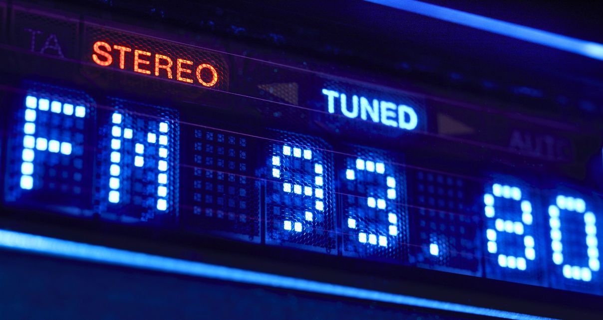 Close-up of a digital radio display showing "FM 93.80" in blue, with "STEREO" in orange and "TUNED" in white, illuminated against a dark background.