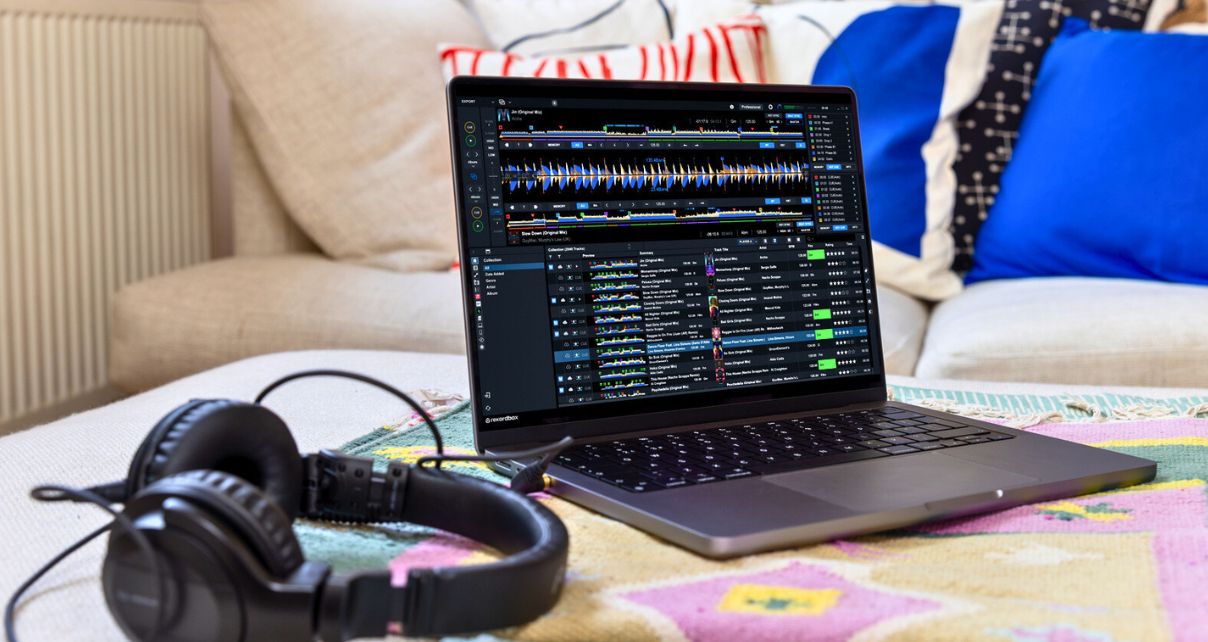 A pair of black headphones sits next to a MacBook Pro laptop in a cozy living room.