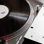 Roundup: The 10 Best DJ Turntables Of 2025 A single silver Technics turntable sits next to a simple DJ mixer. On the record is a plain black record with a white label that says the letter "A".