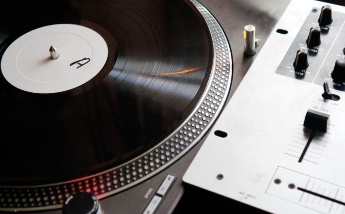 A single silver Technics turntable sits next to a simple DJ mixer. On the record is a plain black record with a white label that says the letter "A".