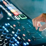 The right hand of a white DJ uses the crossfader on a Rane Four controller in a foggy setting.