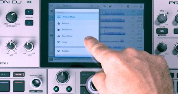 A person points to the display screen of a Denon DJ Prime Go+ unit. There's a list of various music streaming services visible, including Amazon Music, Beatport, and Tidal. 