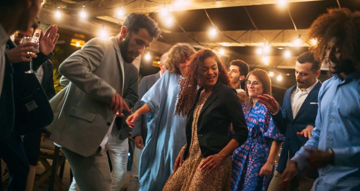 A diverse crowd of people smiling and dancing at a wedding under soft lighting
