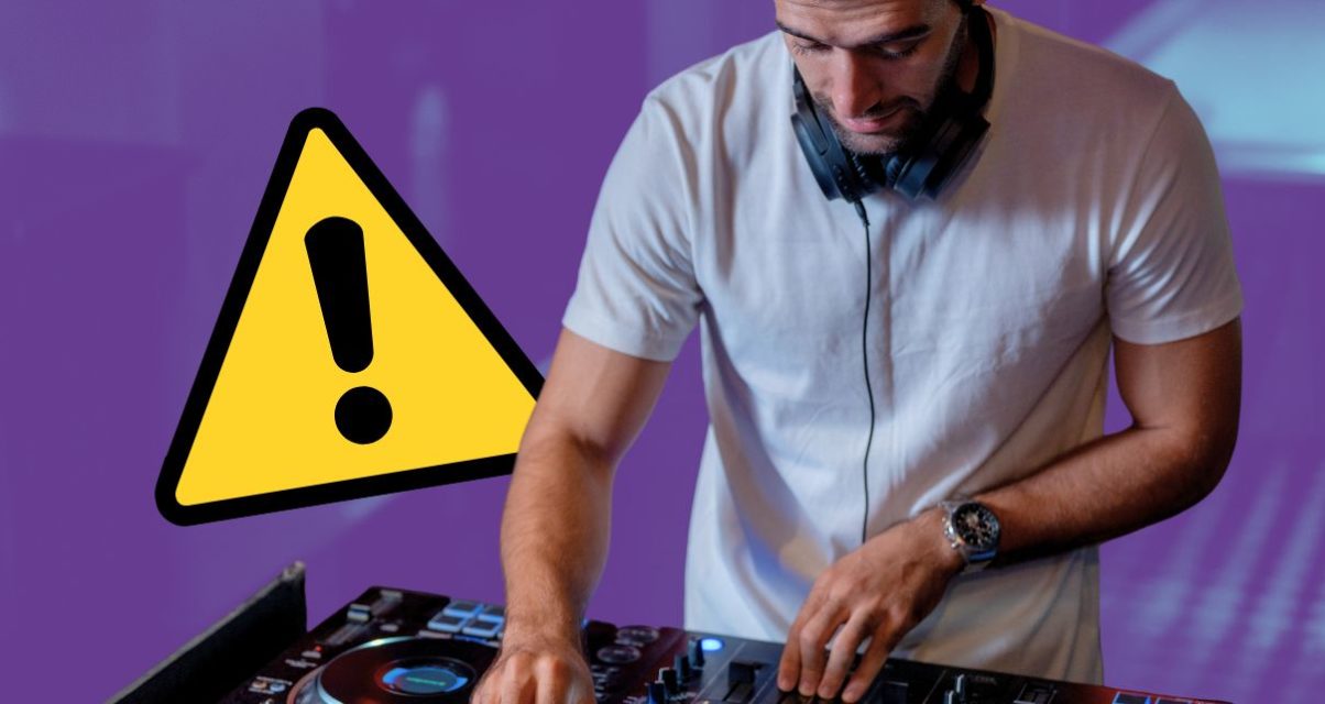 A white man with dark features wears black straight-cabled headphones, a white t-shirt, and a watch. He stands behind DJ gear. There is a purple filter over the background, and to his left is a graphic depicting a bright yellow caution sign.