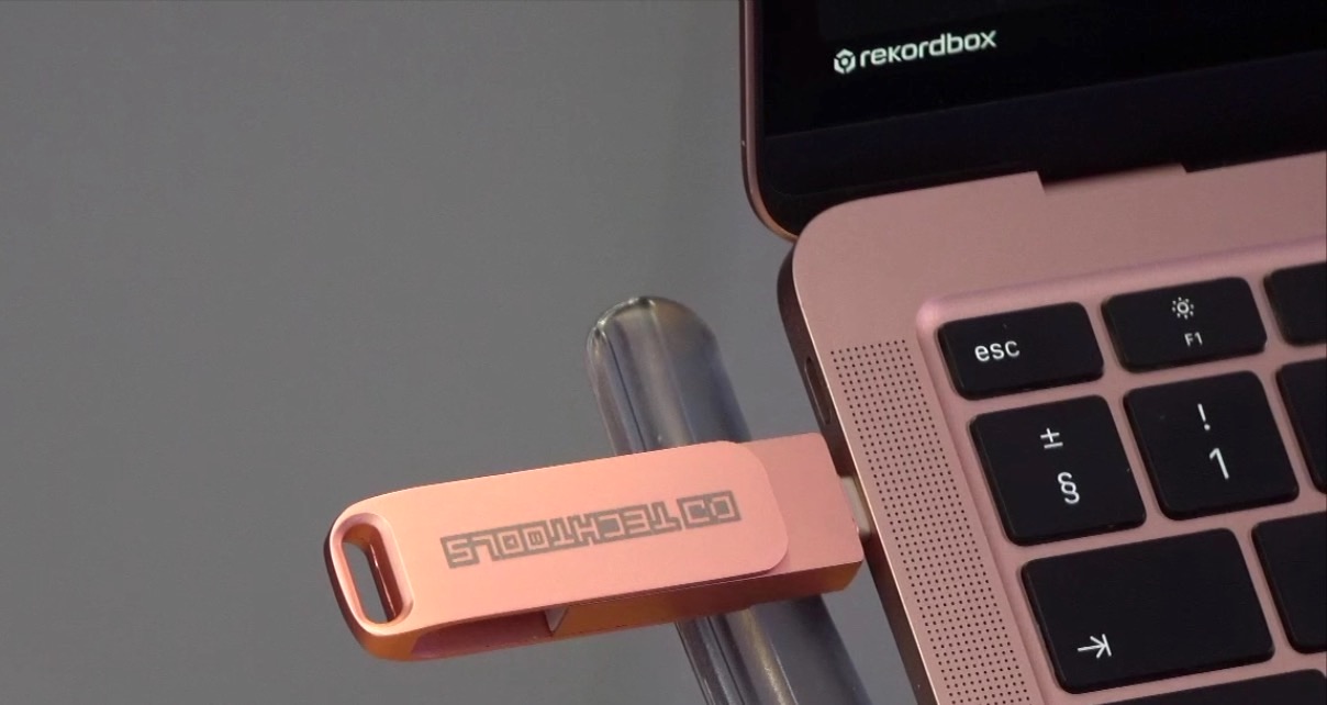 A rose gold DJ TechTools USB drive plugged into a silver MacBook