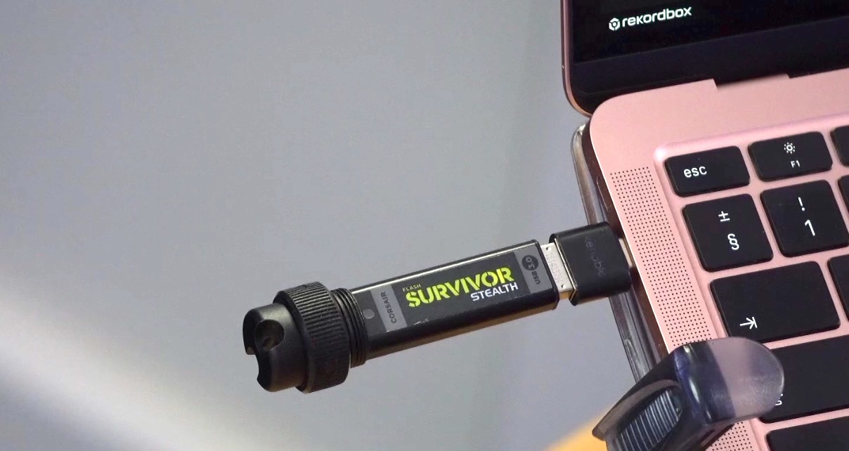 Black and light green Corsair Survivor Stealth USB drive plugged into a silver MacBook Pro.