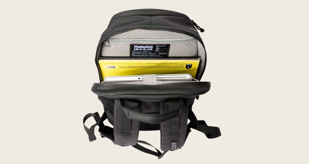 A black Magma Solid Blaze 80 backpack with the main compartment unzipped, showing a laptop and vinyl tucked inside.