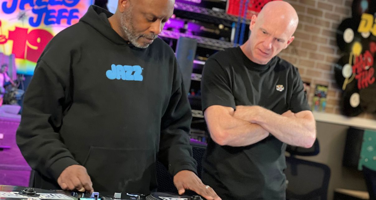Our tutor Steve Canueto, arms crossed, stands next to DJ Jazzy Jeff, watching him scratch records.