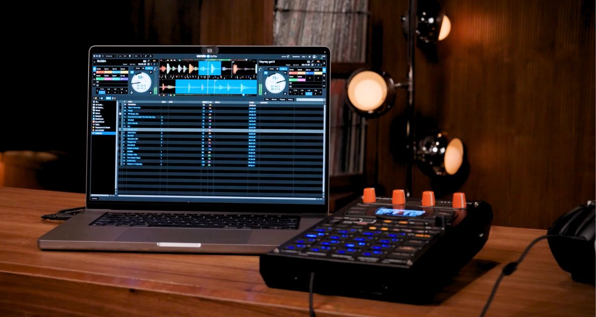 A silver laptop displaying Serato DJ software sits on a wooden table next to a Roland SP-404MKII.