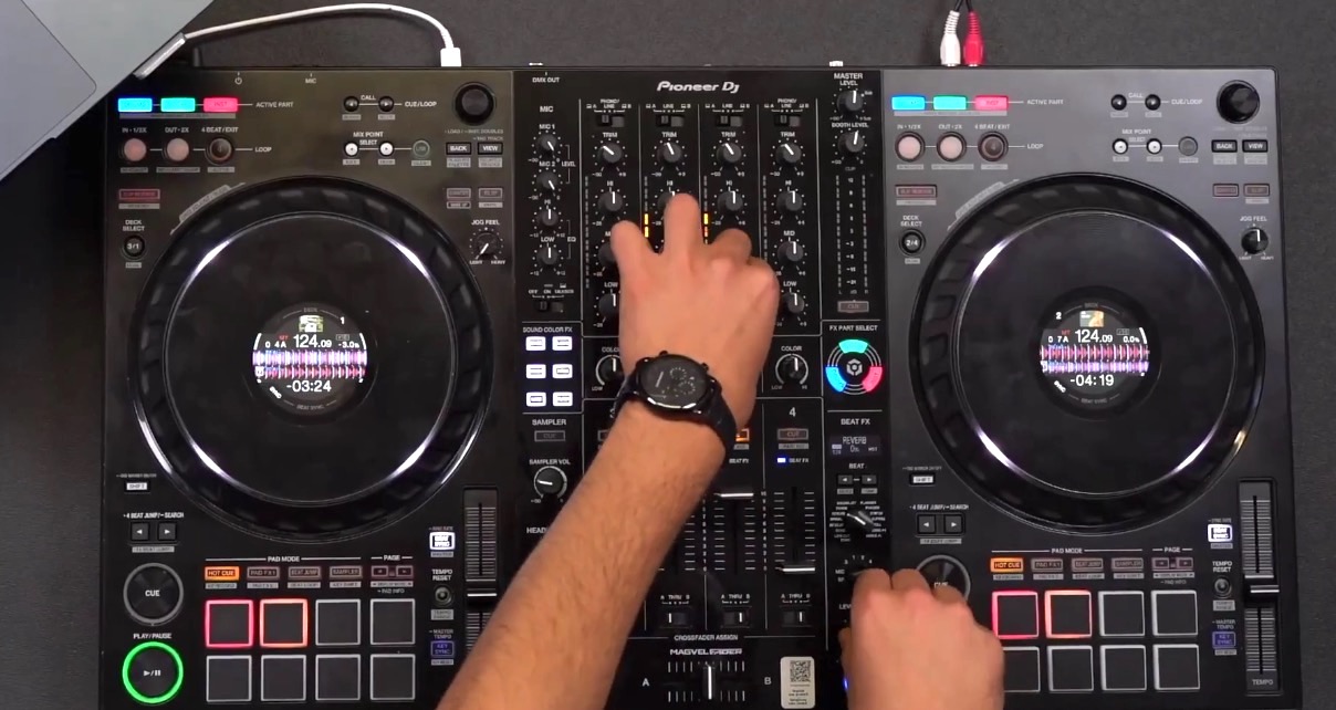 Top-down view of a DJ mixing on a black Pioneer DJ DDJ-FLX10 controller, set against a dark grey table. 