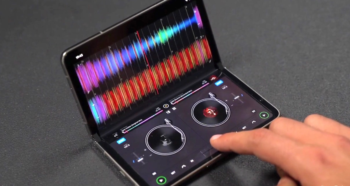 A user interacts with a Pixel Fold device showcasing Djay Pro 5.4 software. The screen features audio waveforms and digital turntables for mixing music. 