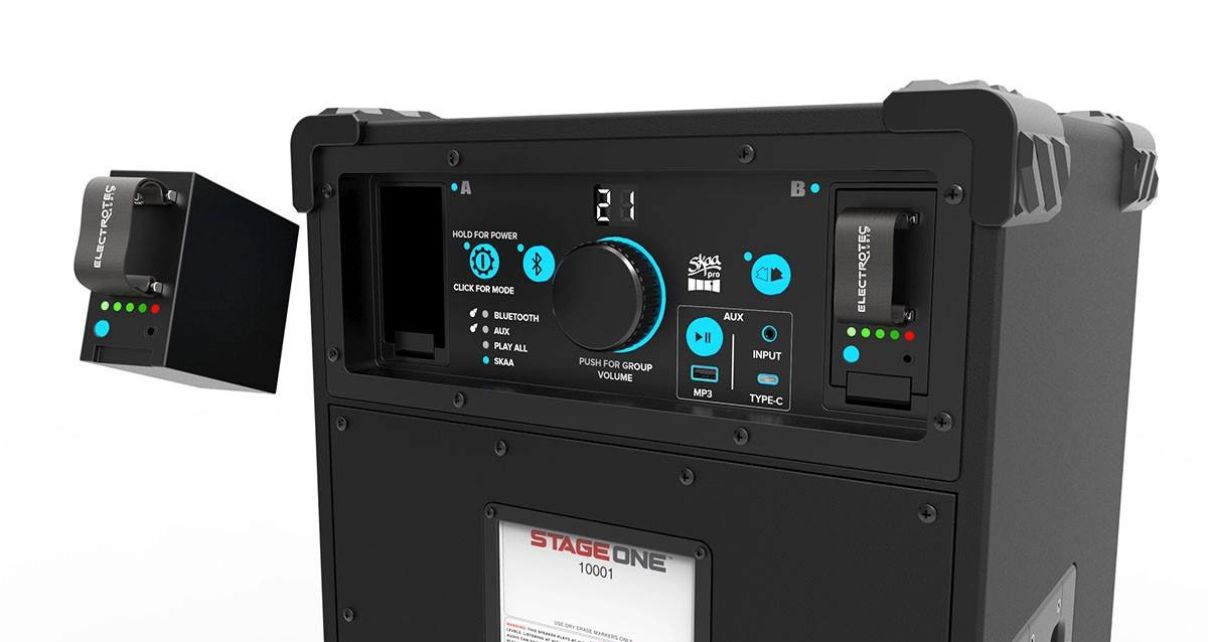 The rear panel on a single black Electrotec Stage One portable speaker, showing a control panel featuring a volume knob, power button, input options, and Bluetooth connectivity indicator. There's also a spare battery highlighted on the left. 