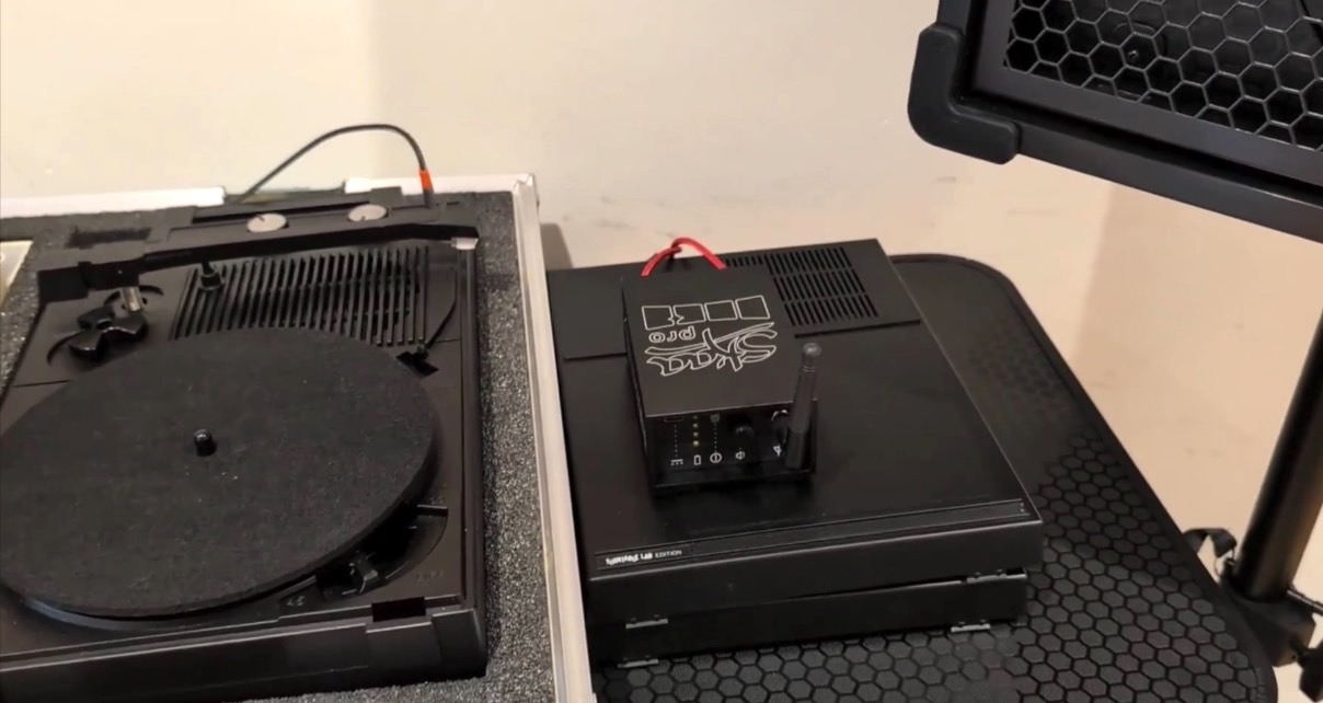 A close-up of a black retro turntable and a SKAA wireless audio transmitter, showcasing a mix of vintage and modern audio equipment. 
