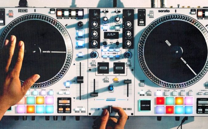 Overhead view of a white Rane One MkII DJ controller. A person is cutting and scratching on the jogwheel and crossfader.