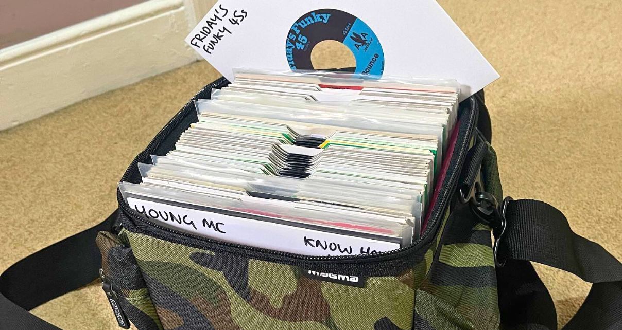 A bunch of 7" records with white sleeves sit in a camo Magma backpack.