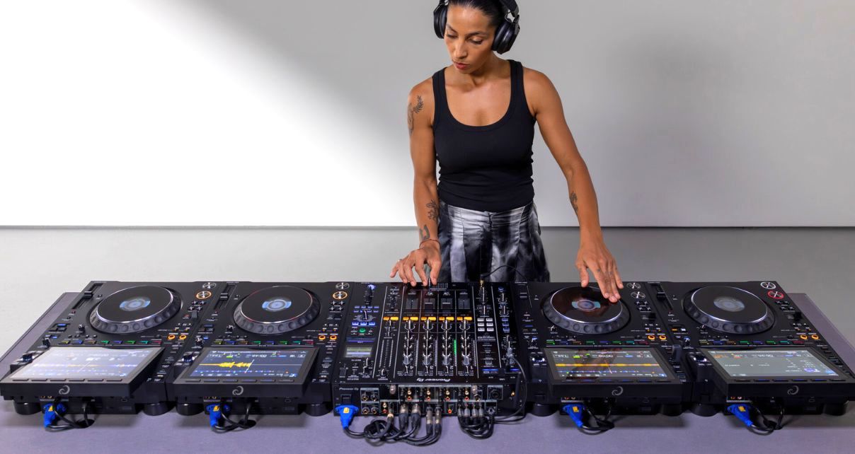 A DJ mixes behind four AlphaTheta CDJ-3000X media players and DJM-A9 in a minimalist studio. 