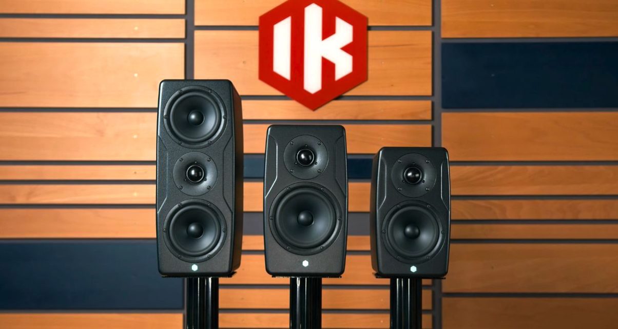 Three sizes of IK Multimedia iLoud Precision MKII Monitors lined up against a wooden wall. There is a red logo with white lettering that says "IK".