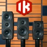 Three sizes of IK Multimedia iLoud Precision MKII Monitors lined up against a wooden wall. There is a red logo with white lettering that says "IK".