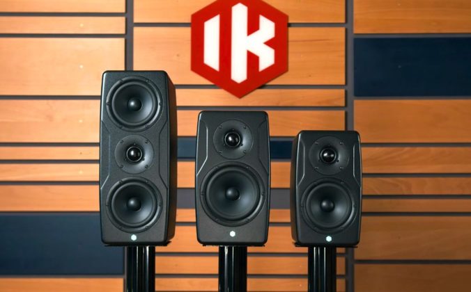 Three sizes of IK Multimedia iLoud Precision MKII Monitors lined up against a wooden wall. There is a red logo with white lettering that says "IK".