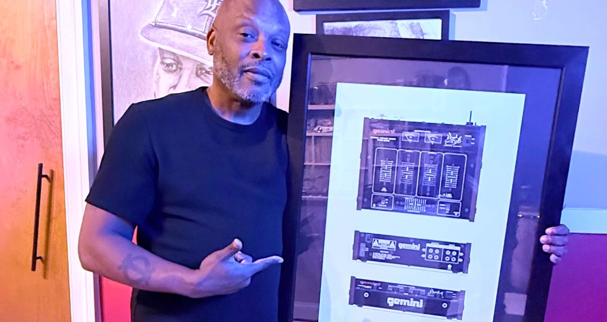 DJ Jazzy Jeff holds and points towards a framed print of a Gemini mixer while smiling at the camera.