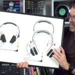 DJ tutor Phil Morse holds a framed illustration of Sennheiser HD-25 headphones with detailed schematic drawings against a white background. Behind him is a large white bookshelf containing various DJ gear, books, and trinkets.