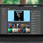 Are Beatport & Beatsource About To Merge? A laptop displays Beatport's pop music section, featuring Carly Rae Jepsen's album and various music charts. It sits on a light wooden desk with a blurry nature background.