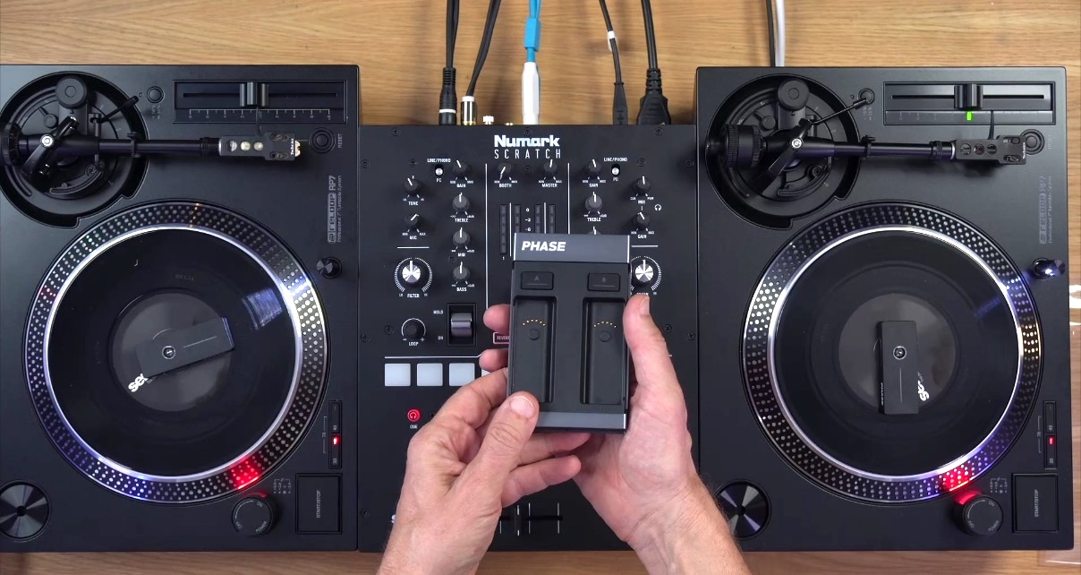 A person holds a Phase wireless control device over a Numark Scratch mixer and Reloop RP-7 turntables, showcasing a compact DVS set-up.
