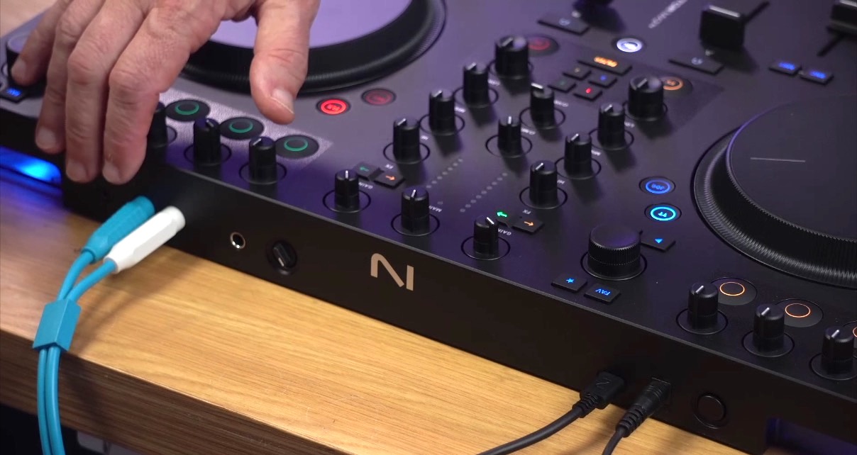 The rear panel of a Traktor MX2 DJ controller. A person gestures towards some connections. 