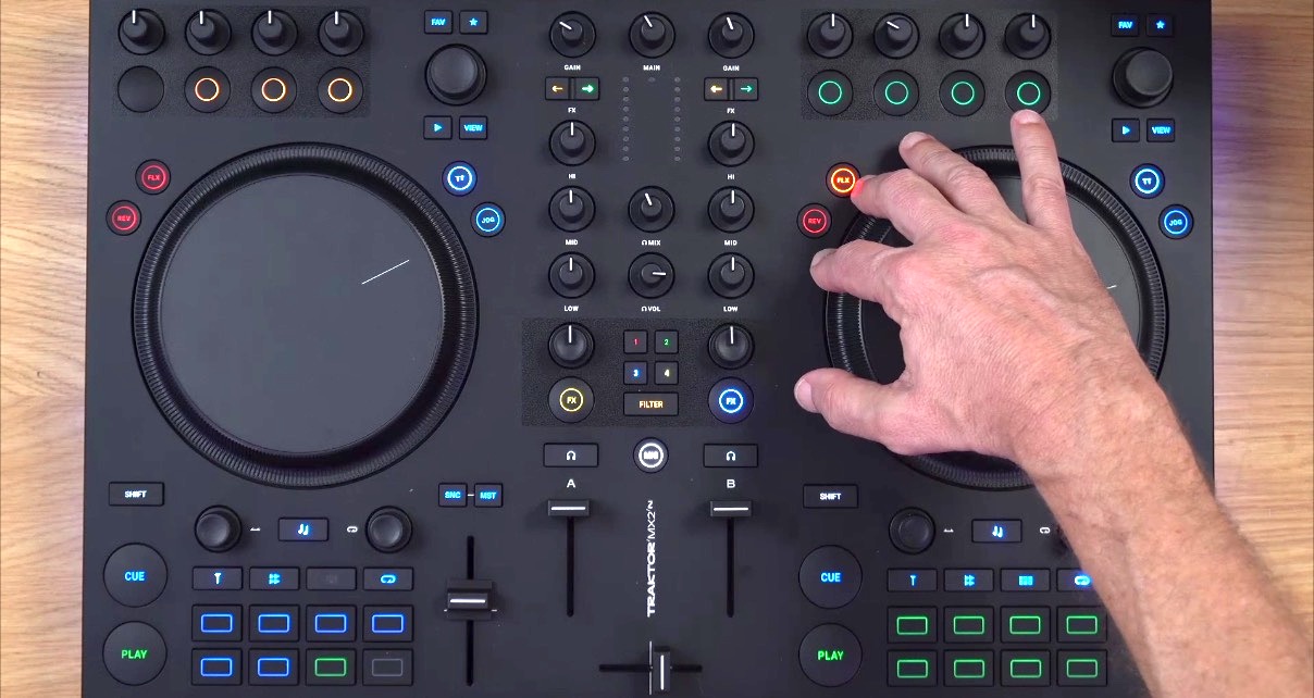 Overhead shot of someone adjusting the jogwheel on a Traktor MX2 DJ controller. The controller is set on a wooden desk and in a well-lit room. 