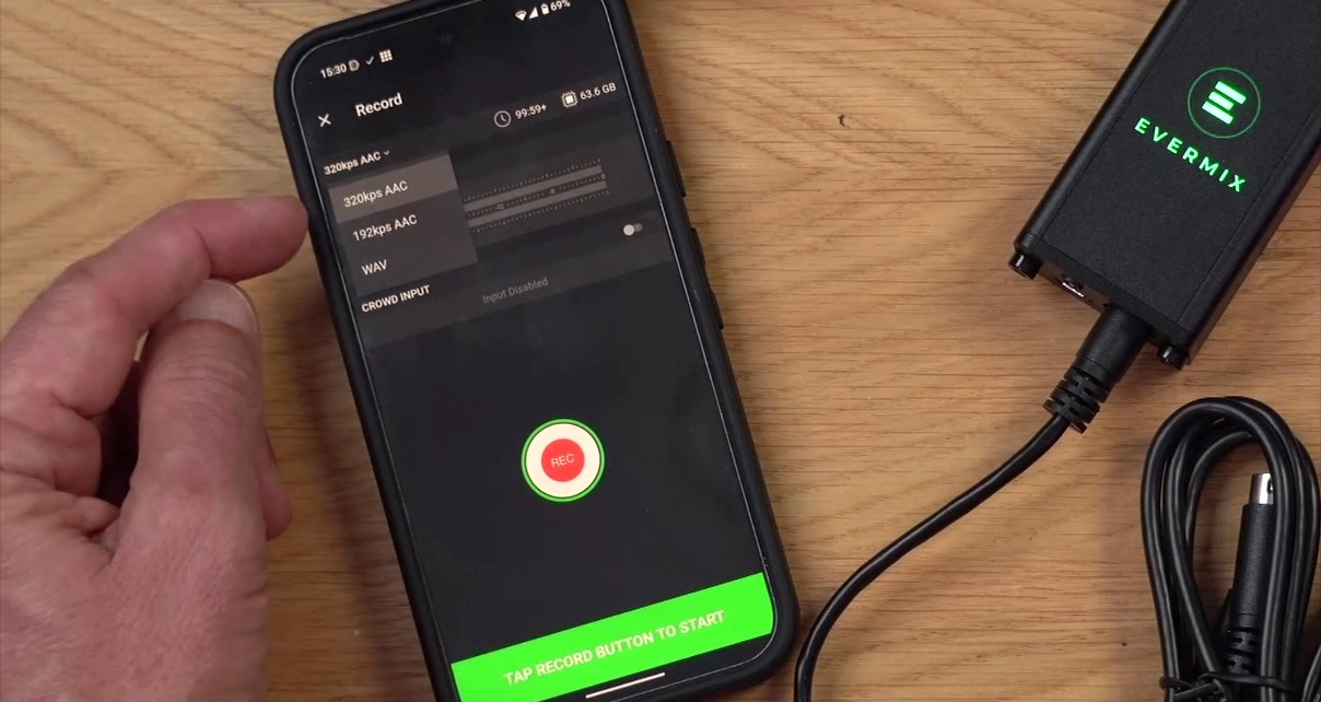 Overhead view of a smartphone and EvermixBox5 device on a light wooden desk. A person is gesturing to the music file format dropdown menu in the Evermix app.