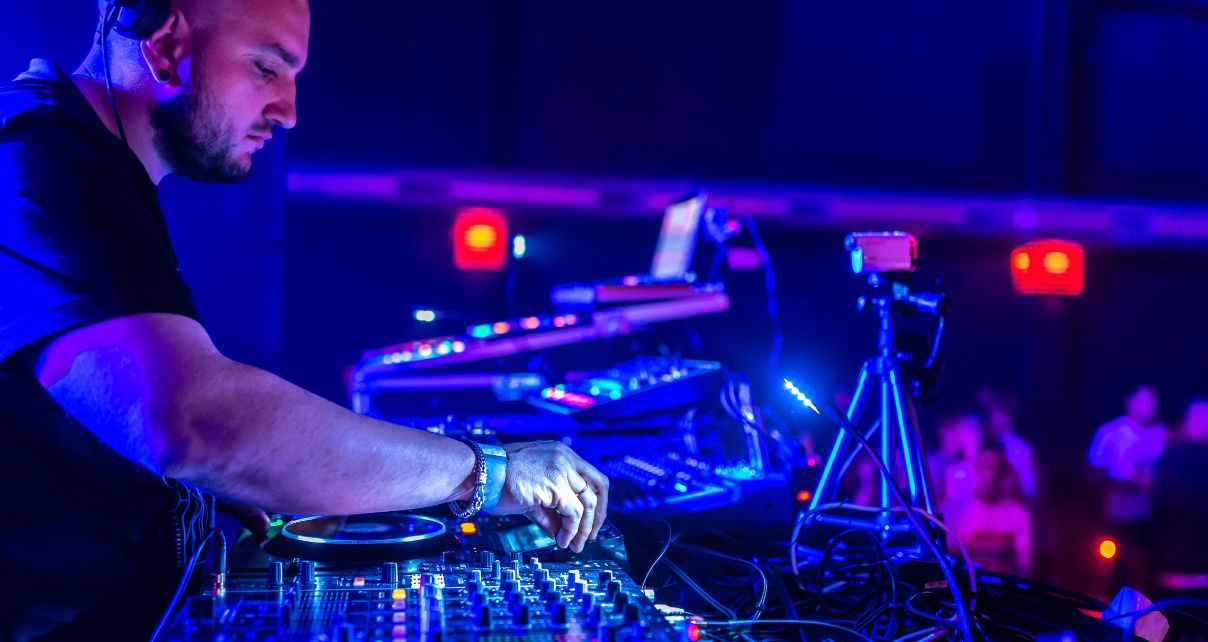 A DJ selects the next track on CDJs in a colourful nightclub environment. 
