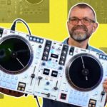 5 Great DJ Set-Ups For Beginners - 2026 Edition A collage design. In the foreground is Phil Morse, who has glasses, shaved hair, and a greying beard. He's holding a white Rane One MkII controller in his hands and smiling at the camera. In the background are four different pieces of DJ gear at 50% transparency. They frame the image in front of a bright yellow background.