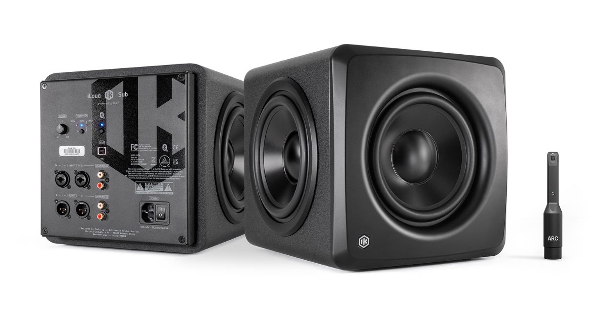 Two IK Multimedia iLoud studio subwoofers and a room calibration mic, all in black. The sub on the left is showing the rear panel, and the one on the right is facing forward.