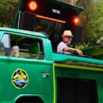 Student Spotlight: The DJ Who Lost Everything Except His Decks A person stands behind DJ gear in a custom-built green and yellow 1978 VW campervan. He's wearing a tan brimmed hat, sunglasses, a light t-shirt, and headphones while adjusting something on the DJ mixer. Behind him are two red lights and speakers.