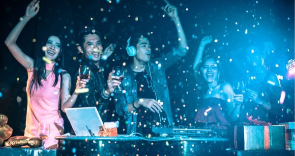 A group of people cheering and celebrating in the DJ booth. They're holding wine glasses and laughing. 