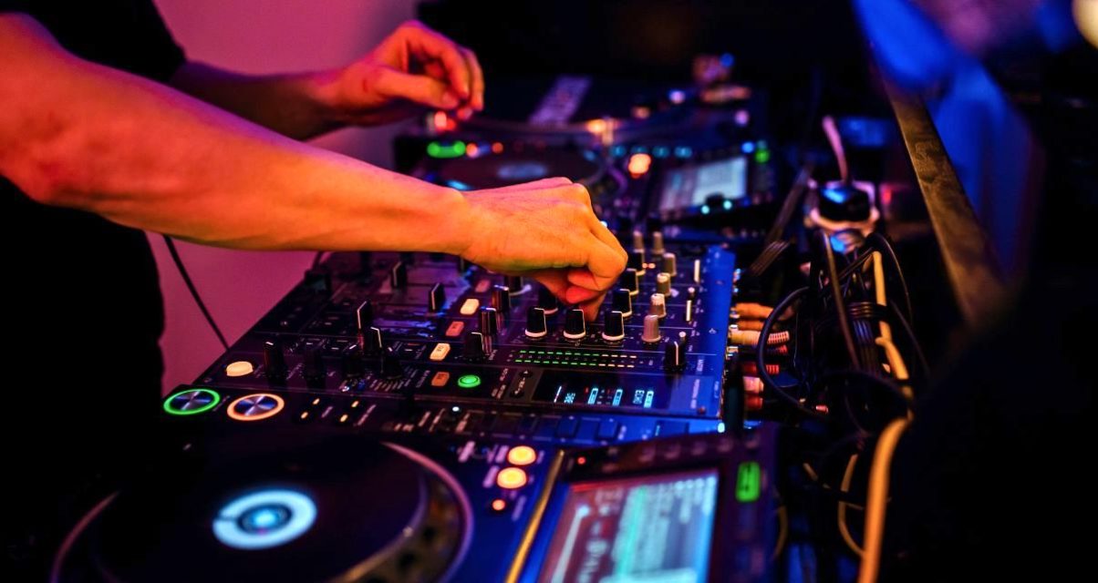 A DJ adjust the EQ on a professional DJ mixer in a nightclub environment.