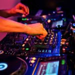 A DJ adjust the EQ on a professional DJ mixer in a nightclub environment.