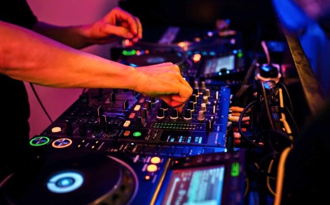 A DJ adjust the EQ on a professional DJ mixer in a nightclub environment.