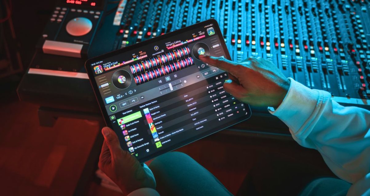 A person sitting at a mixing desk in a recording studio uses Djay Pro with Spotify on a tablet.