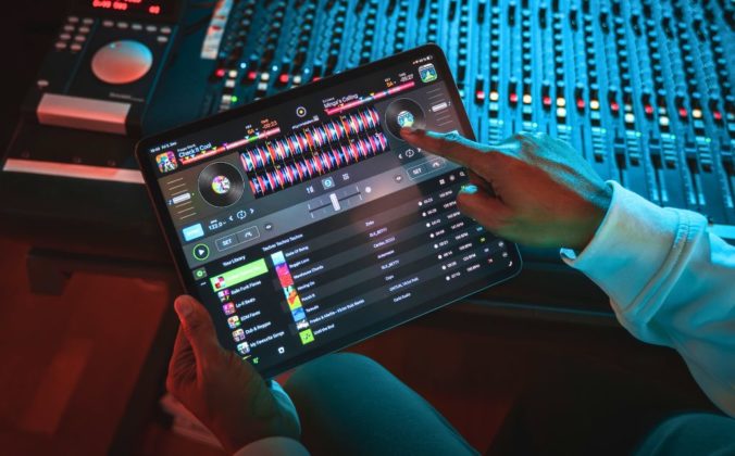 A person sitting at a mixing desk in a recording studio uses Djay Pro with Spotify on a tablet.