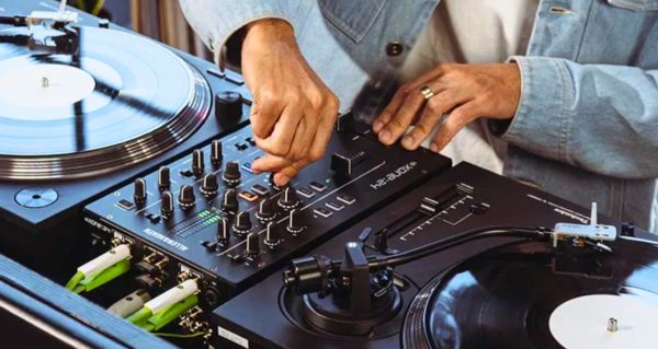 A person wearing a light blue button-up shirt DJs on vinyl and an Allen & Heath Xone:24 mixer. 