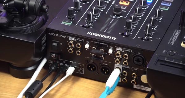 Close-up of an Allen & Heath Xone:24C mixer showing input/output ports and control knobs, with various connected cables. 