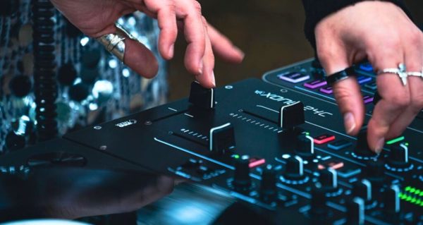 Close-up on an Allen & Heath Xone:24C mixer. A person is DJing with it, adjusting the crossfader and filter. 