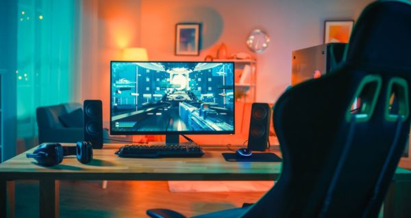 A warm and colourful computer gaming room, showcasing the desktop monitor, headphones, and laptop speakers. 