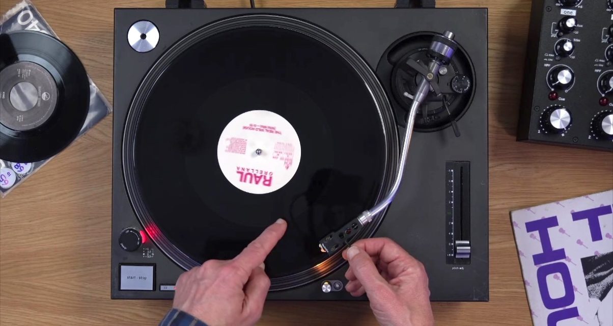 DJ's hands on a Technics turntable demonstrating vinyl mixing techniques from an overhead perspective.