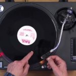 DJ's hands on a Technics turntable demonstrating vinyl mixing techniques from an overhead perspective.