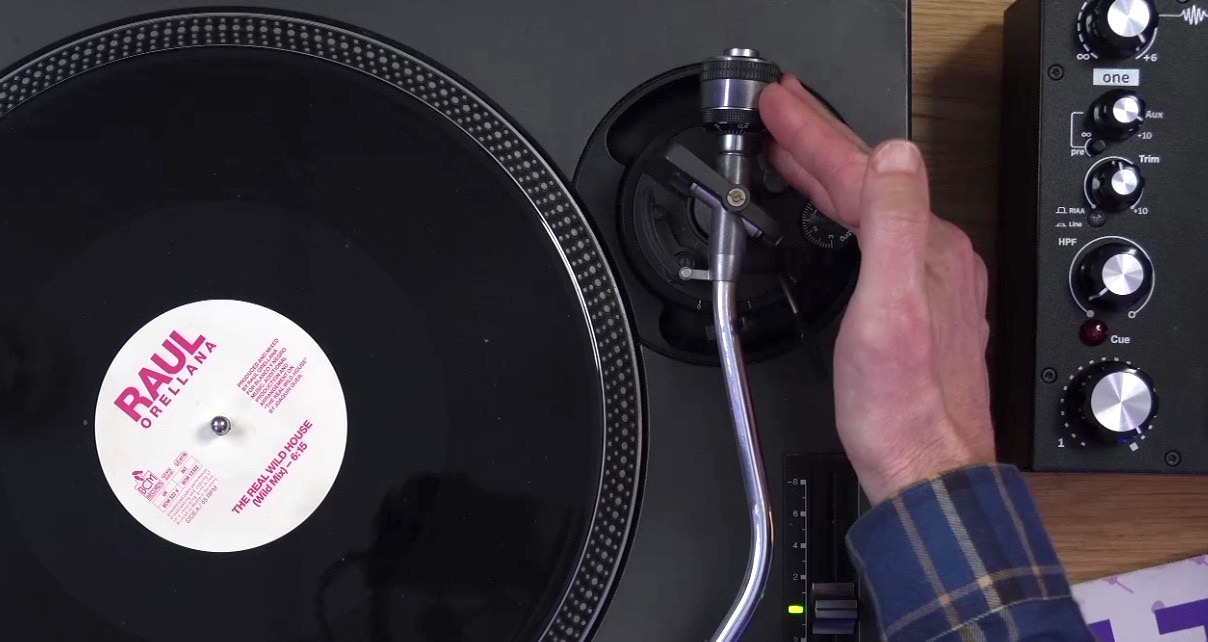 Close-up of a DJ's hand adjusting the counterweight on a Technics turntable tonearm with a vinyl record on the platter. 
