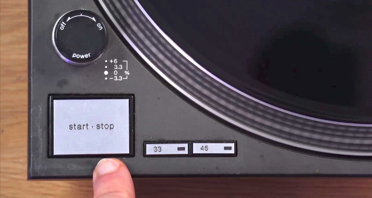 Close-up of a Technics turntable showing the power on/off dial, start/stop button, and 33/45 speed selector buttons. 