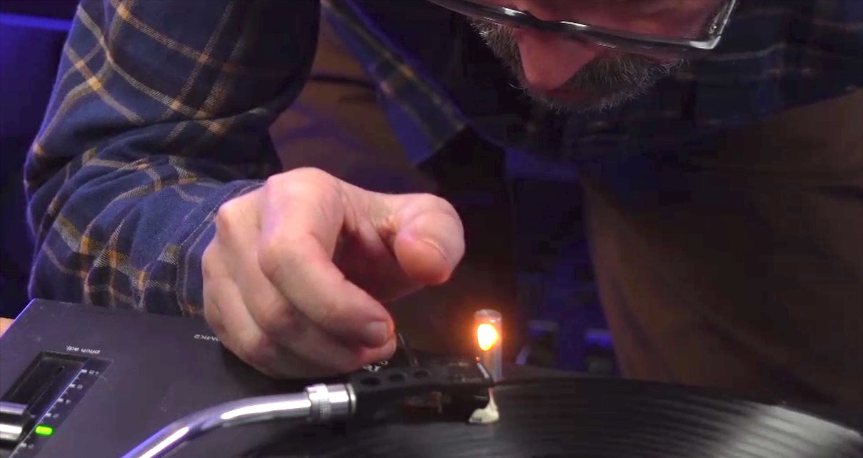 DJ examining vinyl grooves up close using the turntable's pop-up light in a dimly lit environment. 