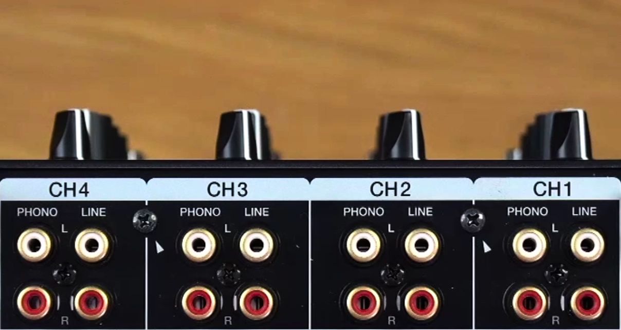 Close-up of professional DJ mixer back panel showing four channels with phono and line RCA inputs, with white left and red right sockets for each input type. 